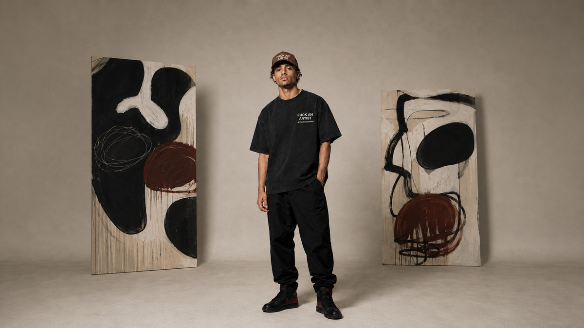 A man wearing a black Quiet Power t-shirt, black pants, and a cap stands between two large abstract canvas paintings in a minimalist studio setting.
