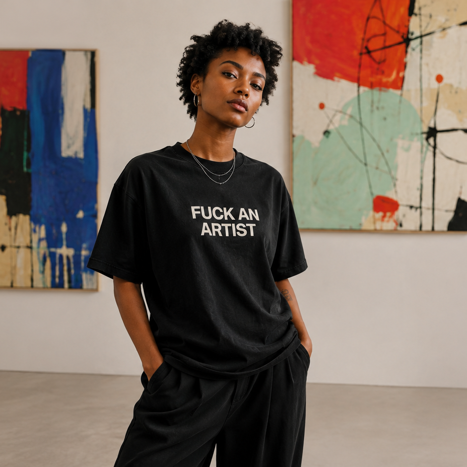 A model wearing a black graphic t-shirt with the text 'FUCK AN ARTIST' in white, standing in a gallery space with abstract paintings on the wall.